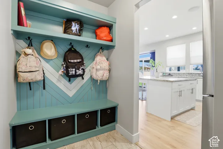 Built-in mudroom bench with chevron-patterned millwork, upper storage shelf, matte black hooks, and lower cubbies, featuring wood-finish flooring in the surrounding space and white cabinetry with a stone-top kitchen island