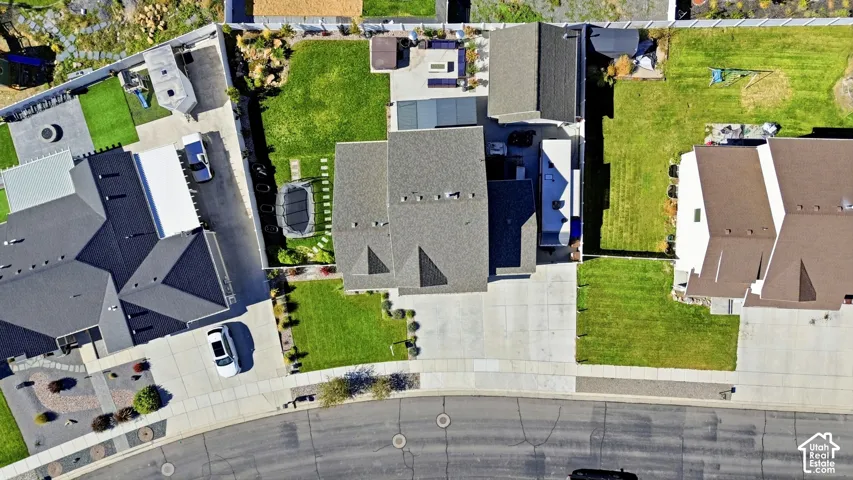 Aerial view of property featuring a concrete driveway, multi-gabled shingle roof, manicured lawn, and hardscaped rear patio