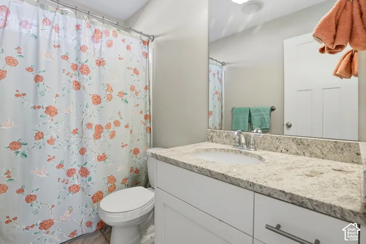 Bathroom featuring a vanity with stone-finish countertop, undermount sink, chrome faucet, shaker-style cabinetry, and large wall-mounted mirror
