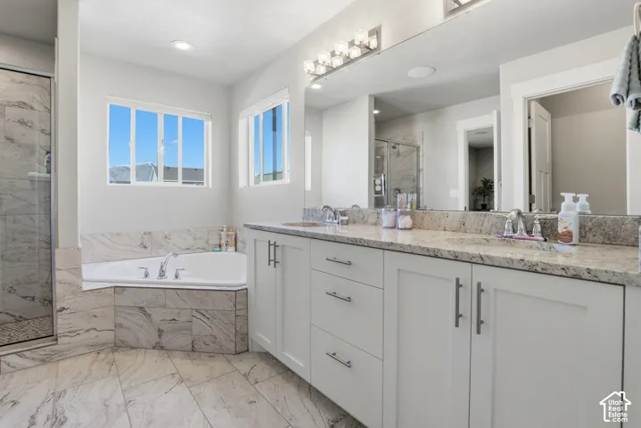 Dual-sink vanity with stone countertops, corner soaking tub, and tile-surround walk-in shower