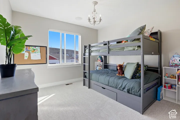 Bedroom featuring neutral carpeting, a dual-pane sliding window, and a decorative chandelier light fixture