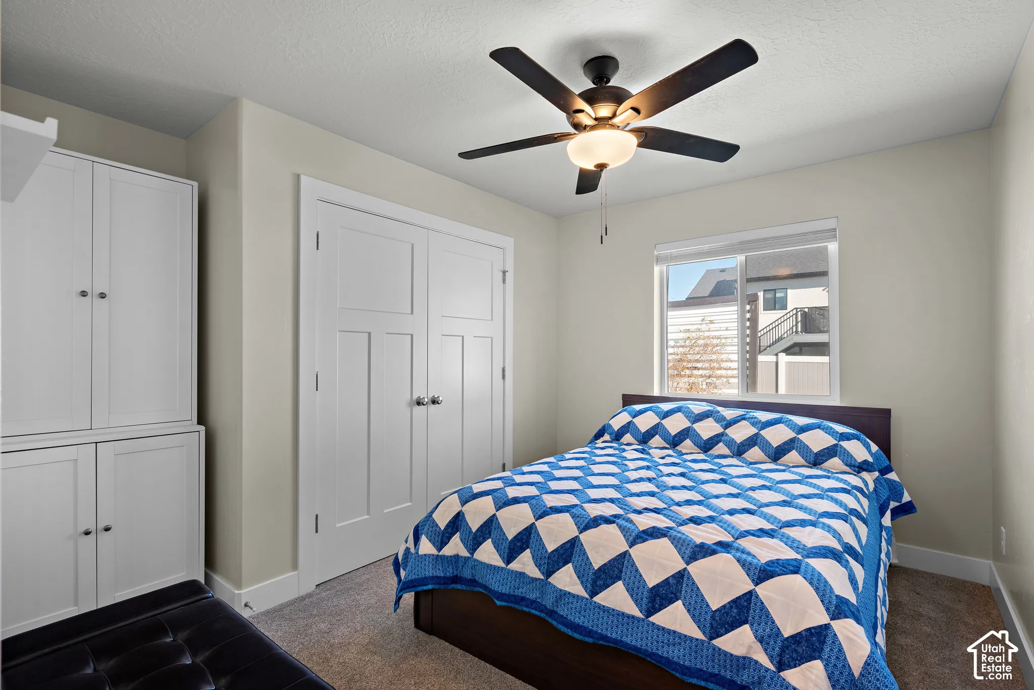 Room featuring neutral wall tones, carpeted flooring, built-in white cabinetry, dual-panel closet doors, and a ceiling fan with integrated lighting