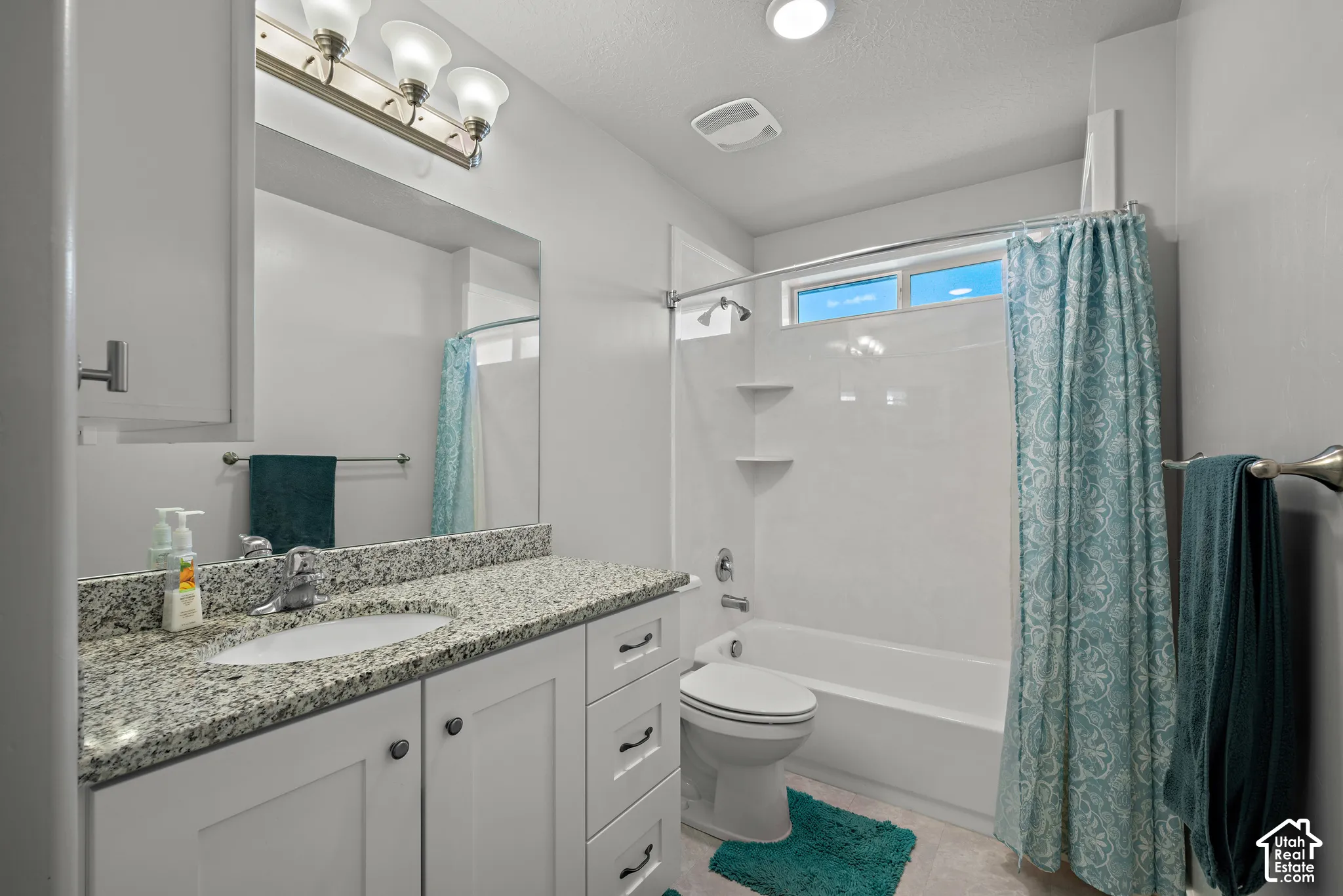 Bathroom featuring a white shaker-style vanity, stone-patterned countertop, integrated oval sink, and a tub-shower combination with built-in shelving
