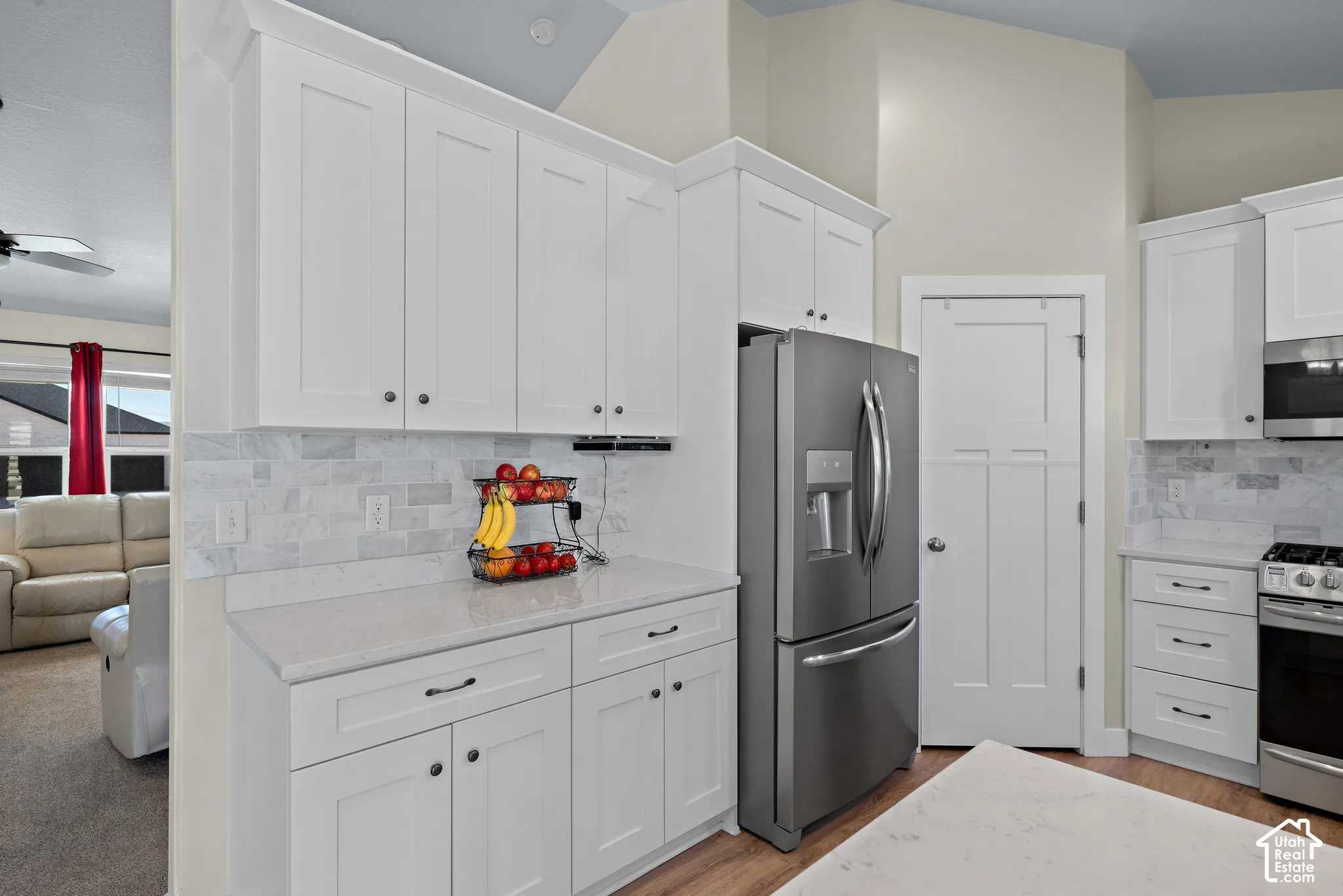 Kitchen featuring white cabinetry, stone-finish countertops, stone tile backsplash, stainless steel appliances, and vaulted ceilings