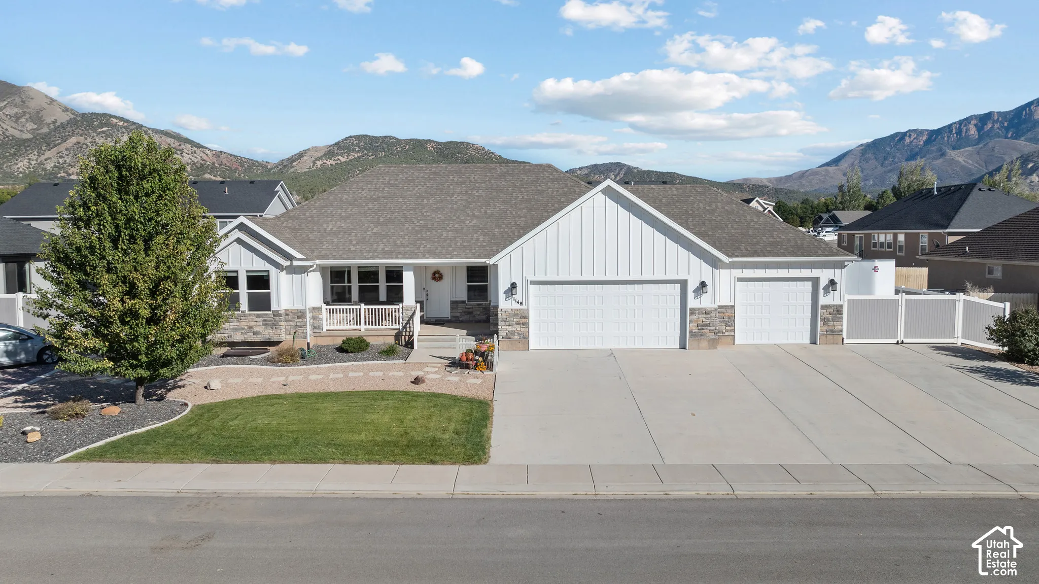 Single-level exterior featuring board and batten siding, stone masonry accents, a three-car garage, and mountain scenery
