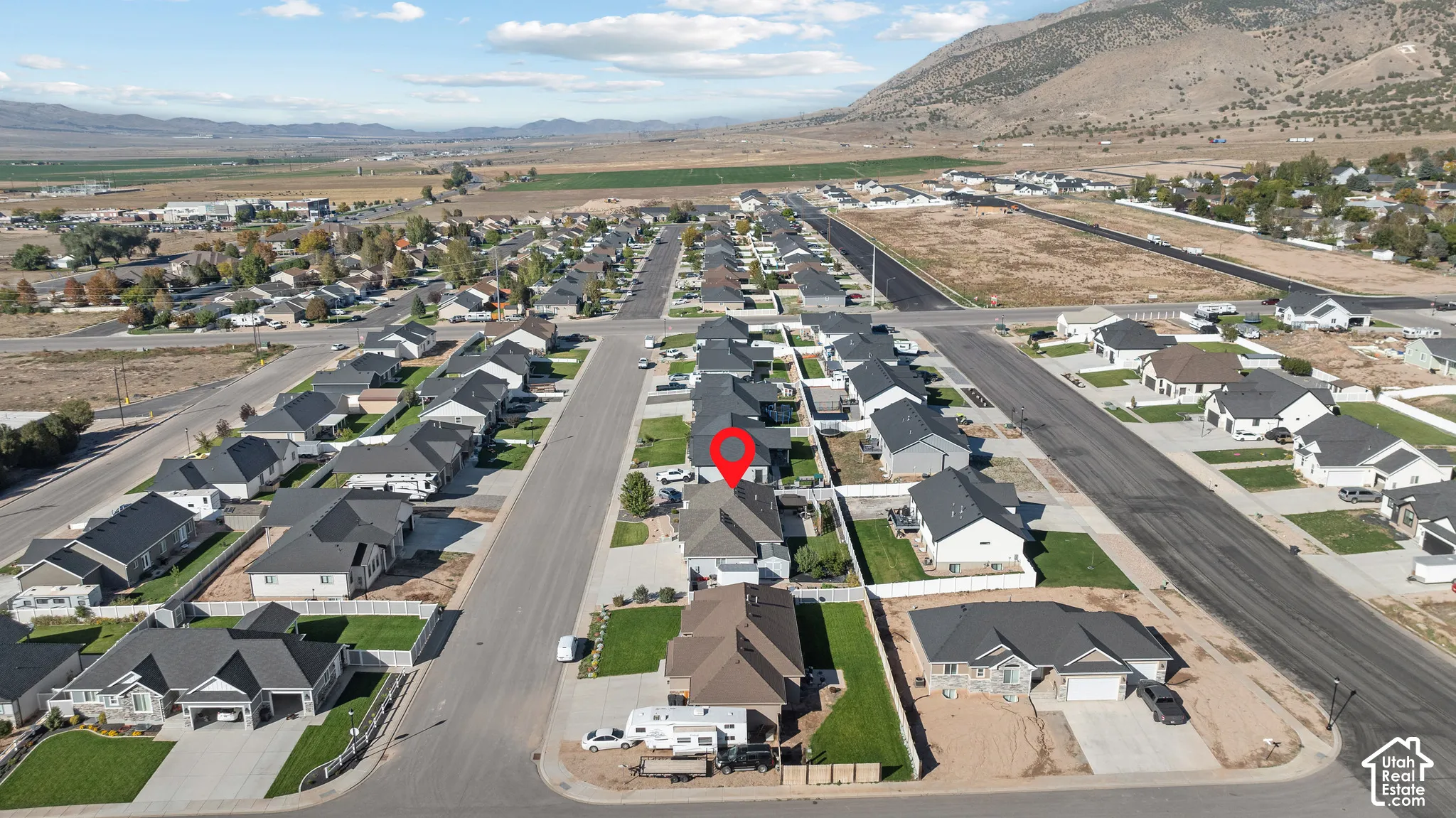 Aerial perspective of residential property featuring a pitched roofline, attached garage, concrete driveway, and surrounding mountain backdrop