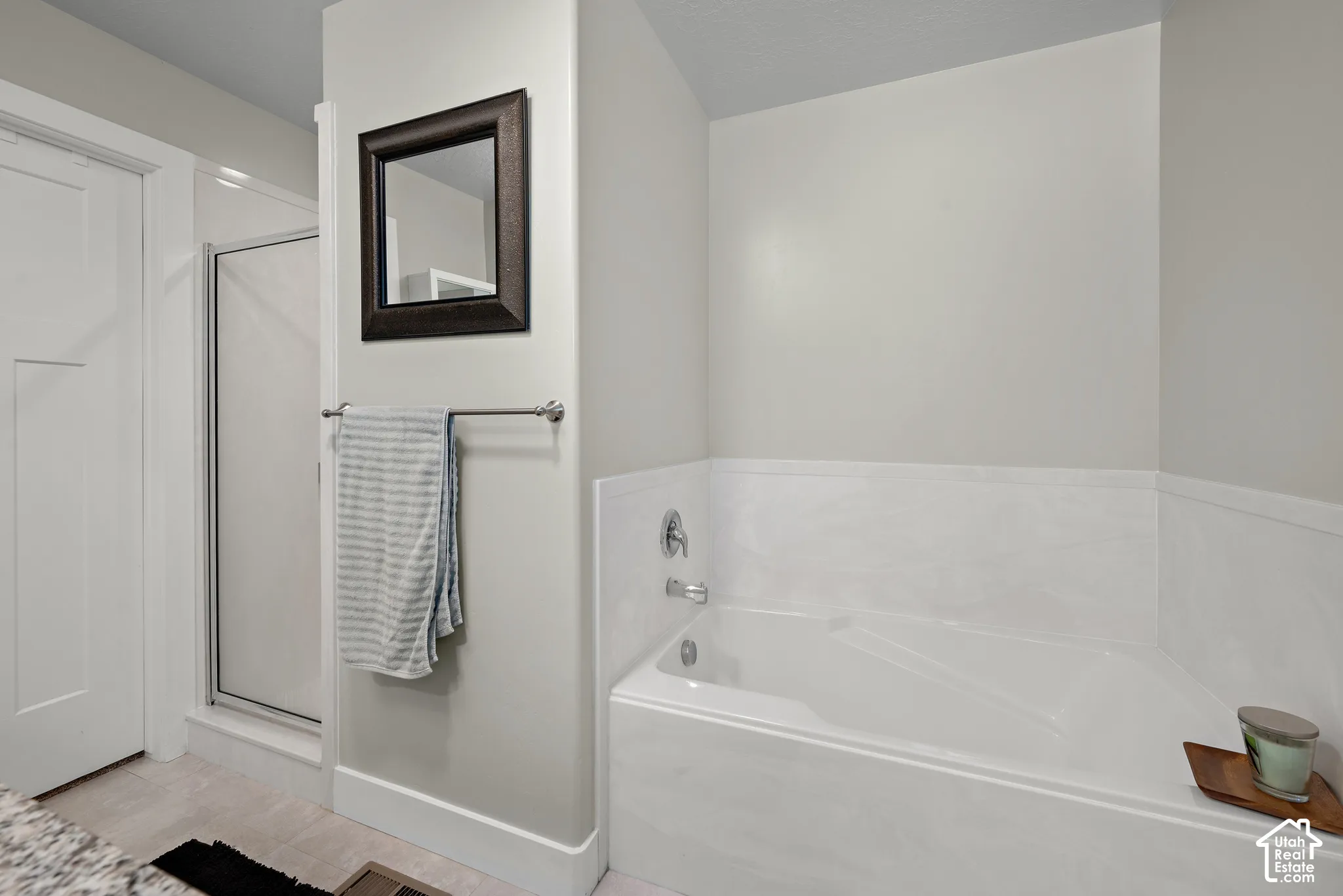 Soaking tub with a white surround, separate glass-enclosed shower, wall-mounted mirror, and metal towel bar