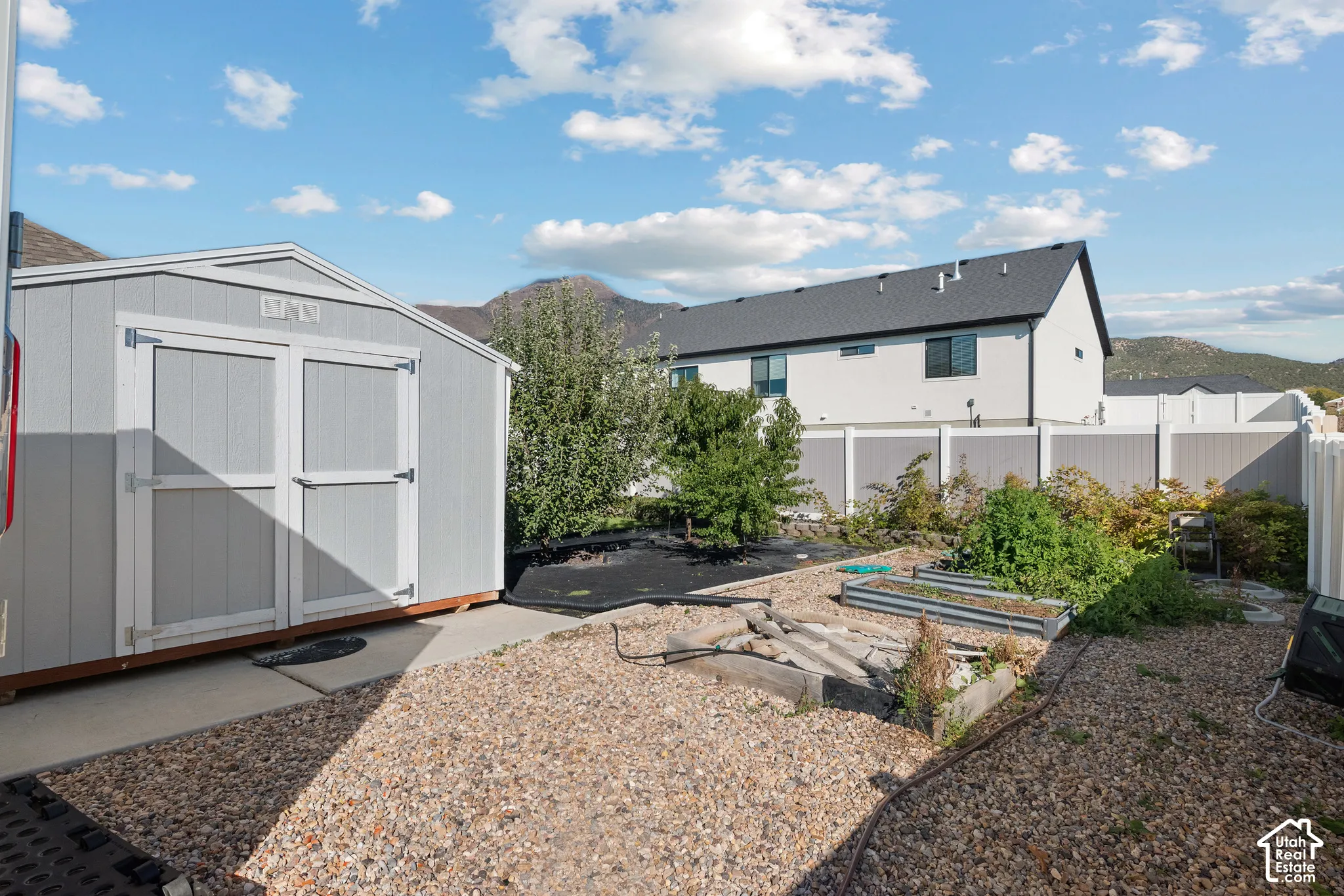 Backyard featuring a gray detached storage shed, raised metal garden beds, gravel ground cover, and a white privacy fence