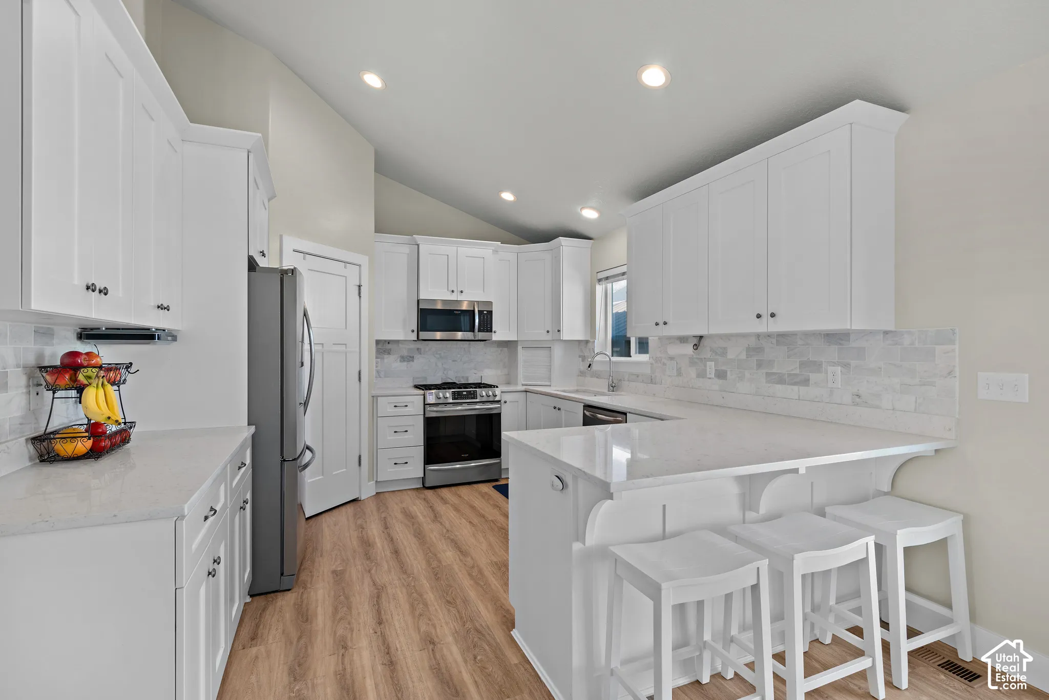 Kitchen featuring white shaker-style cabinetry, solid-surface countertops, stone tile backsplash, stainless steel appliances, and wood-finish flooring
