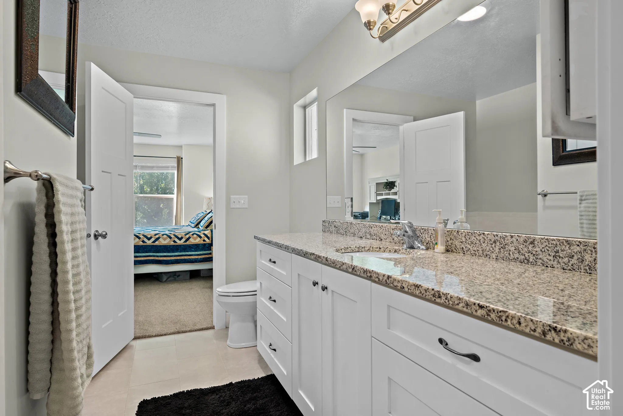 Bathroom vanity featuring white shaker-style cabinetry, stone-finish countertop, undermount sink, chrome faucet, and expansive wall-mounted mirror