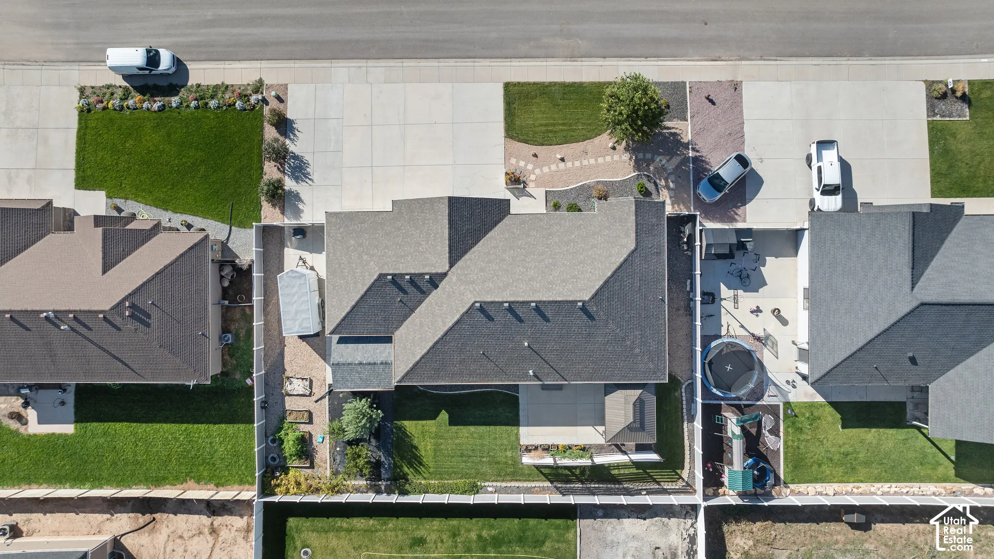Aerial perspective of a property featuring an expansive backyard, manicured lawn, concrete patio, perimeter privacy fencing, and a multi-pitch shingle roof