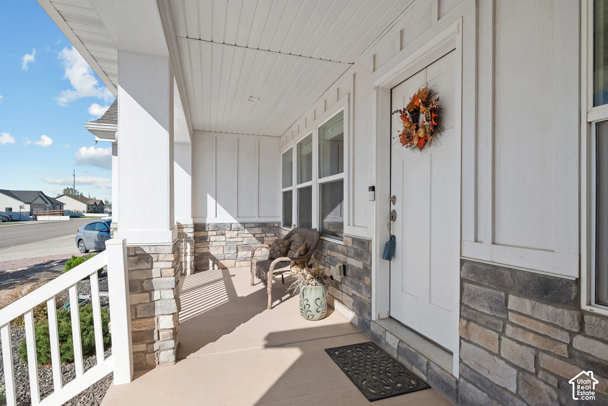 Covered front porch featuring board-and-batten siding, stacked stone veneer accents, and white railing