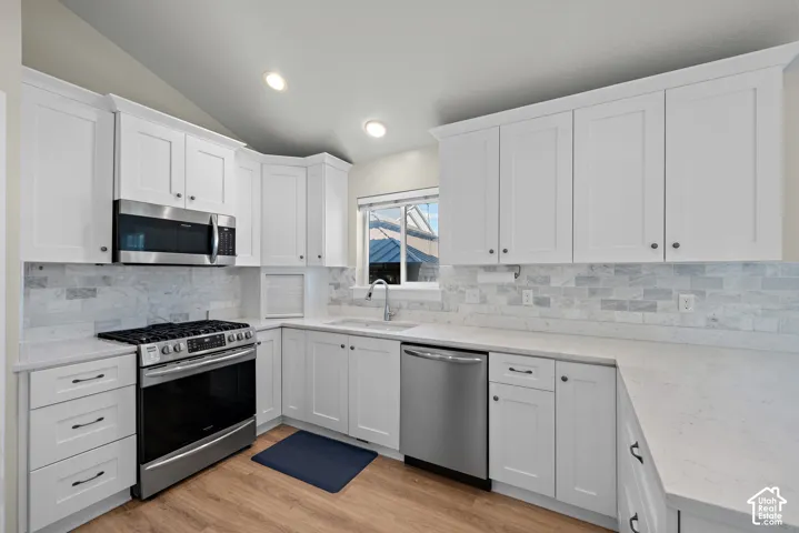 Kitchen featuring white shaker-style cabinetry, solid-surface countertops, stone-tile backsplash, stainless steel appliances, and wood-finish flooring