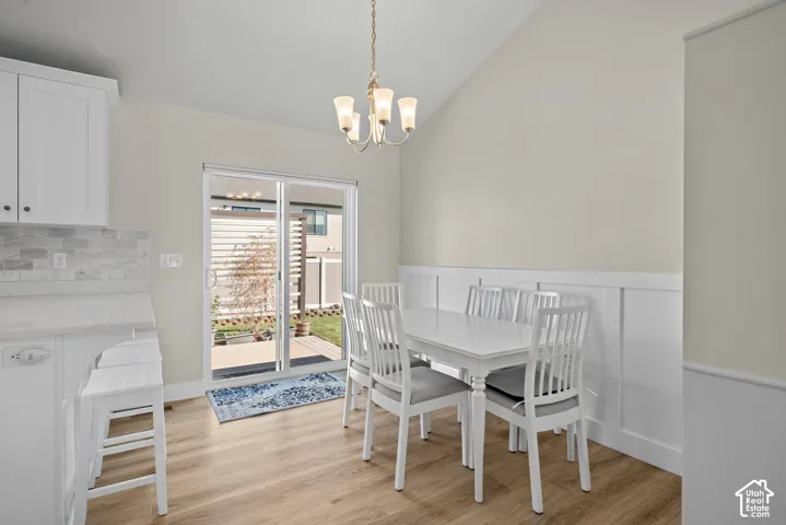 Vaulted ceilings, wood-finish flooring, white board-and-batten wainscoting, sliding glass door, and overhead chandelier
