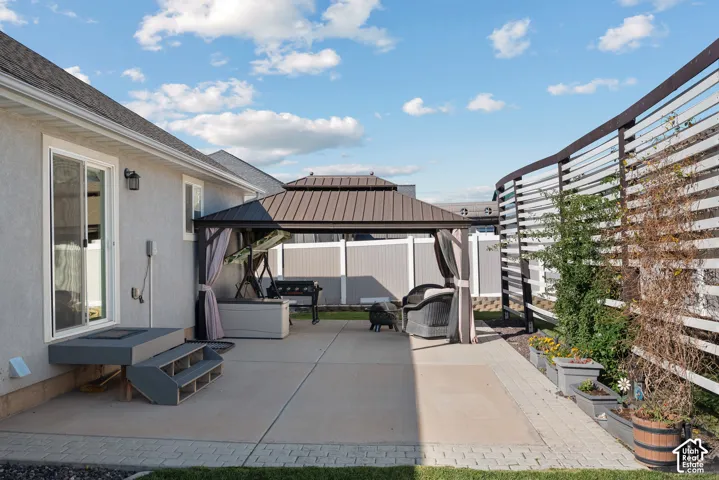 Backyard patio featuring concrete surfacing with decorative paver borders, a permanent metal-roofed gazebo, and custom slatted privacy screening