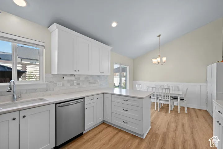 Kitchen featuring white shaker-style cabinetry, solid-surface countertops, stone tile backsplash, wood-finish flooring, and vaulted ceilings with a three-light chandelier