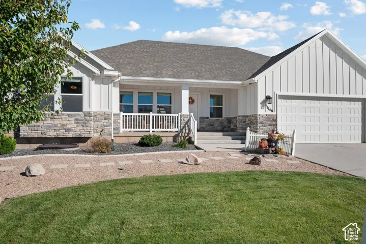 Exterior featuring white board-and-batten siding, stone masonry accents, a covered front porch with white railing, and an attached two-car garage