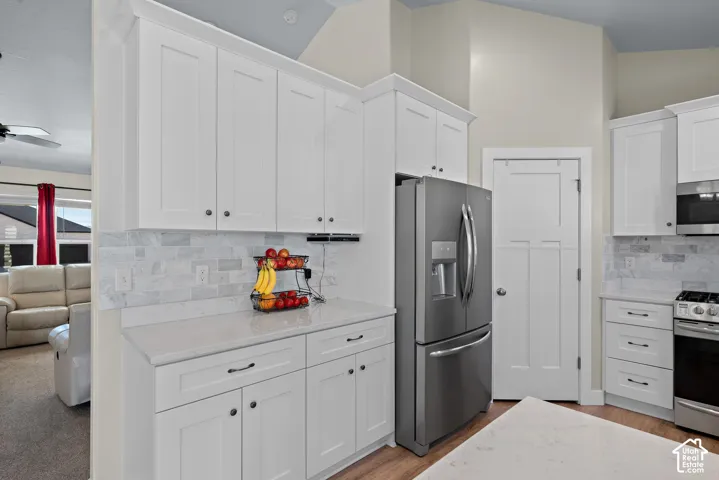 Kitchen featuring white cabinetry, stone-finish countertops, stone tile backsplash, stainless steel appliances, and vaulted ceilings