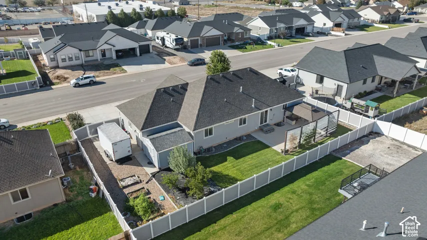 Aerial perspective of a property featuring a fully fenced backyard, manicured lawn, paved concrete patio, and a detached storage structure