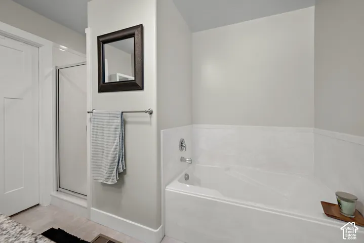 Soaking tub with a white surround, separate glass-enclosed shower, wall-mounted mirror, and metal towel bar