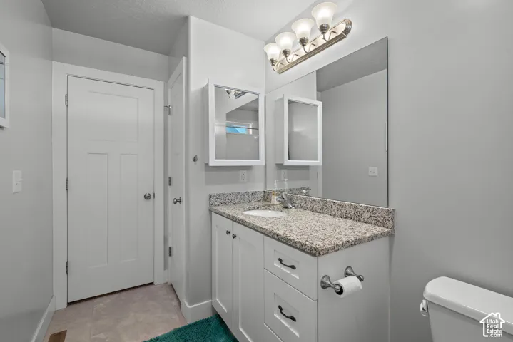 Bathroom featuring a white shaker-style vanity with stone-finish countertop, undermount sink, built-in medicine cabinet, and four-light overhead fixture