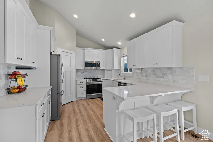 Kitchen featuring white shaker-style cabinetry, solid-surface countertops, stone tile backsplash, stainless steel appliances, and wood-finish flooring