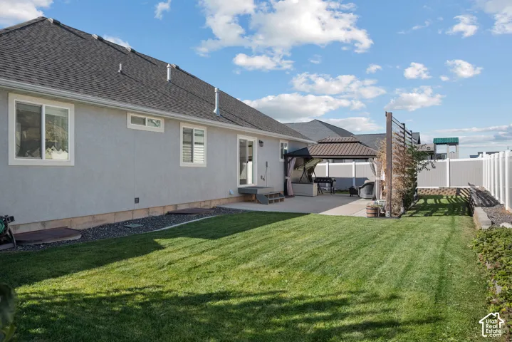 Rear exterior featuring light-colored stucco siding, asphalt shingle roofing, a concrete patio, and a privacy fence