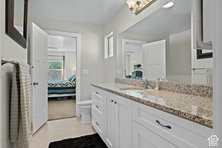 Bathroom vanity featuring white shaker-style cabinetry, stone-finish countertop, undermount sink, chrome faucet, and expansive wall-mounted mirror