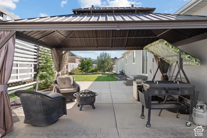 Outdoor living space featuring a metal-frame gazebo with a peaked roof, concrete patio, and decorative privacy screen