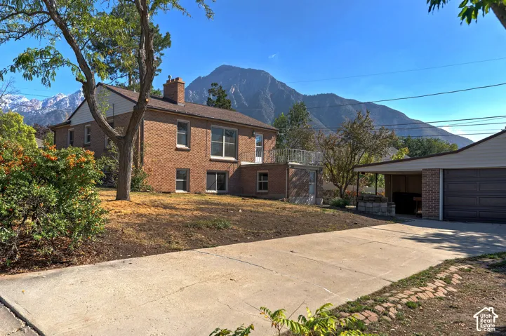 Brick exterior, concrete driveway, detached garage, elevated balcony, and mountain backdrop