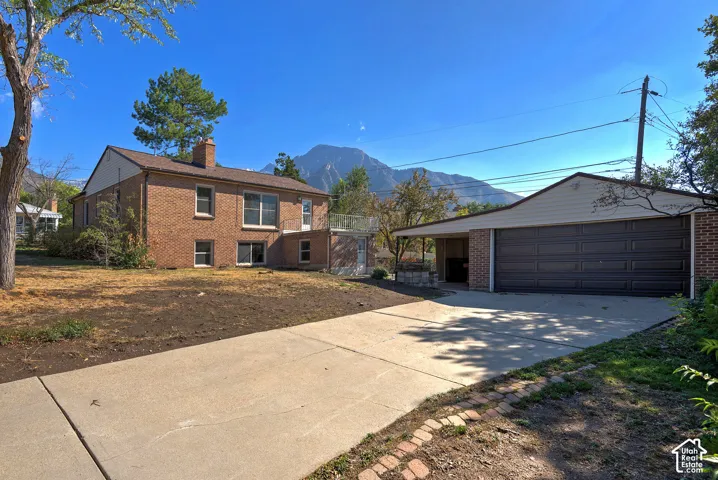 Brick exterior residence featuring an elevated deck, detached garage, concrete driveway, and prominent mountain backdrop