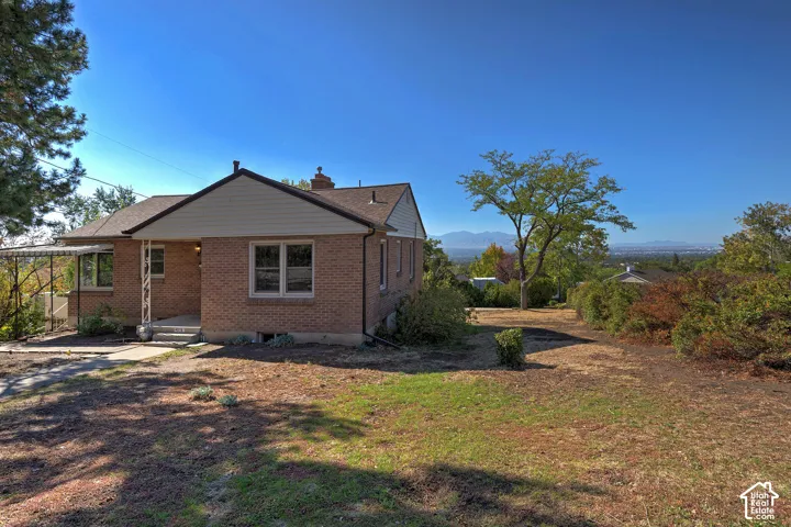 Brick exterior with horizontal siding, covered porch, and expansive lot featuring mature trees and mountain scenery