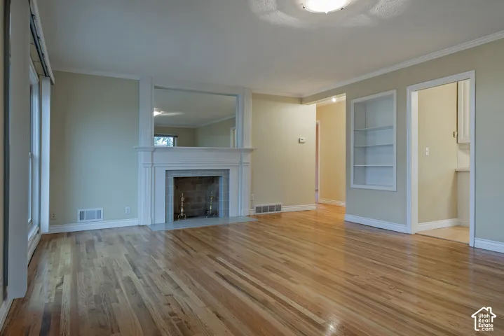 Hardwood flooring, wood-burning fireplace with tile surround, white mantel, integrated mirror, and built-in shelving unit