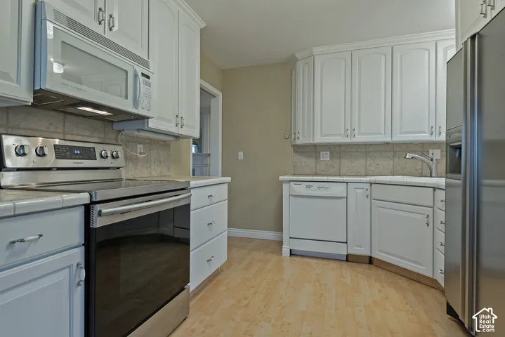 Kitchen featuring white cabinetry, wood-finish flooring, stainless steel appliances, and tile backsplash
