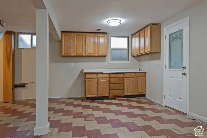 Custom cabinetry featuring upper and lower wood-finish units with countertop surface, geometric patterned tile flooring, flush-mount ceiling lighting, and a white exterior-style door with decorative glass paneling