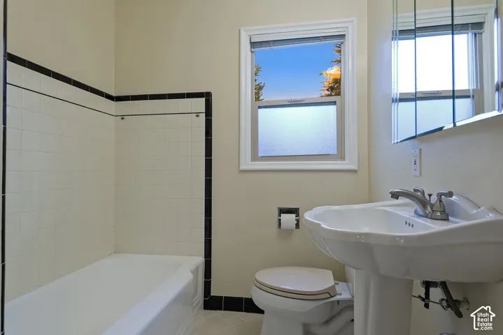 Bathroom featuring a pedestal sink, white porcelain tub with integrated tile surround, black decorative accent tile trim, and a built-in medicine cabinet with mirrored doors