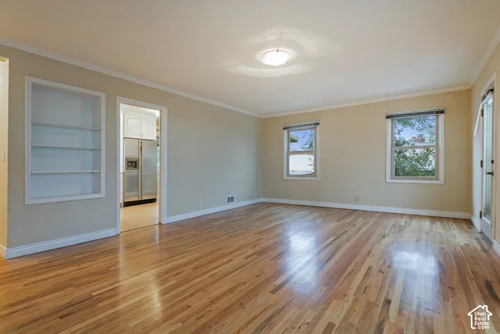 Living area featuring wood-finish flooring, recessed built-in shelving, crown molding, and two windows with blinds