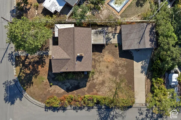 Aerial perspective of a corner lot property featuring an asphalt shingle roof, a detached garage, a concrete driveway, a chimney, and a raised wooden deck