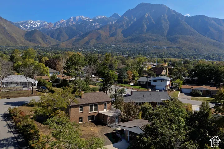 Aerial perspective featuring a two-story brick exterior, shingled roofing, mature trees, and a mountain range backdrop