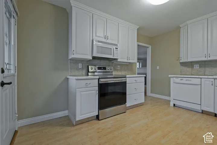 Kitchen featuring white cabinetry, wood-finish flooring, tiled backsplash, stainless steel range with integrated microwave, and white dishwasher