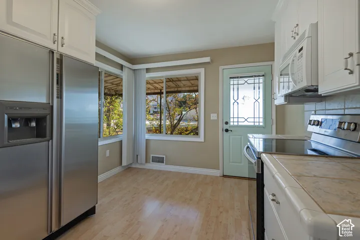 Kitchen featuring white shaker-style cabinetry, stainless steel appliances, tiled countertops, wood-finish flooring, and a glass-paneled exterior door