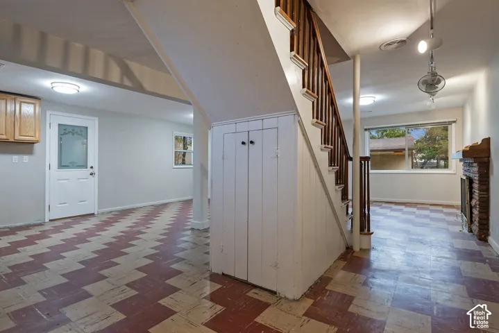 Interior space featuring checkered flooring, a wood-railing staircase with integrated under-stair storage, a masonry hearth, and an exterior door with decorative glass inlay
