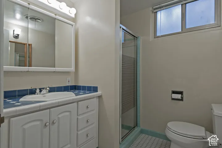Bathroom featuring a white vanity cabinet, tiled countertop with integrated basin, mirrored medicine cabinet, shower enclosure with glass door, and a horizontal window