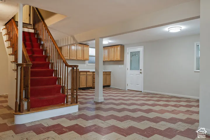 Open-concept area featuring light-tone wood cabinetry, a staircase with a wooden handrail, a paneled exterior door with decorative glass, and geometric patterned flooring