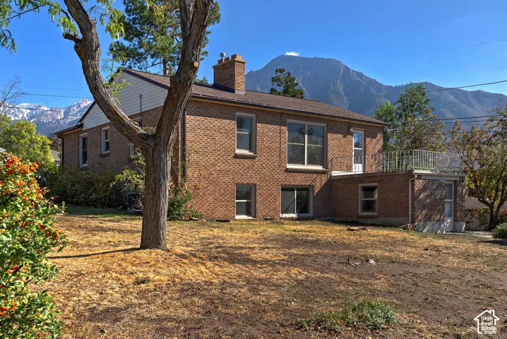 Brick exterior featuring a chimney, metal-railed elevated deck, and a mountainous backdrop