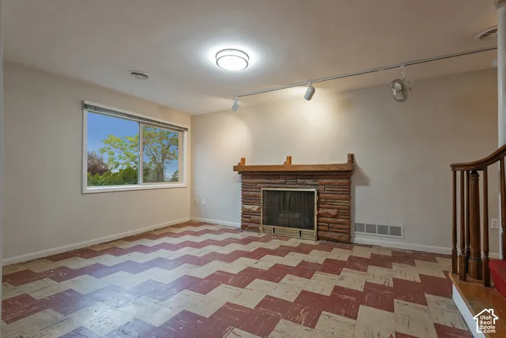 Living area featuring a masonry fireplace with a wood mantel, multi-colored patterned flooring, track lighting, and a staircase with a wooden balustrade