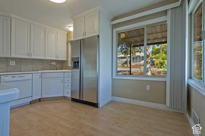 Kitchen featuring white cabinetry, wood-finish flooring, tile backsplash, stainless steel refrigerator, and large picture windows