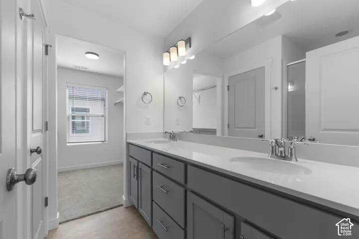 Dual-sink vanity with a solid-surface countertop, cabinetry featuring shaker-style doors, polished chrome fixtures, and a wall-to-wall vanity mirror