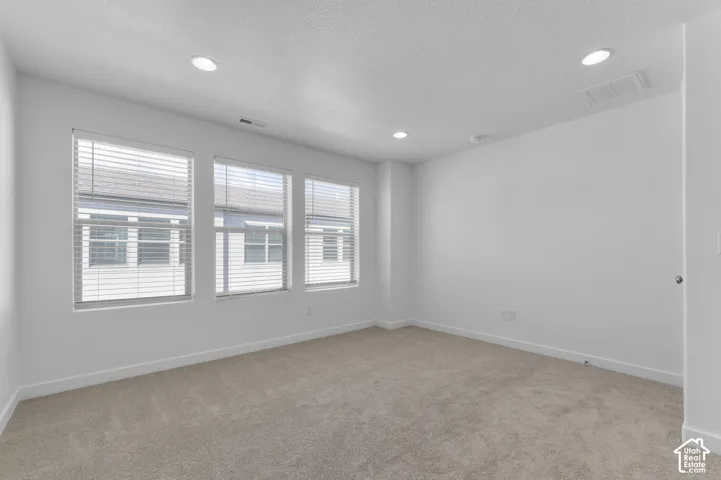 Neutral-toned carpet, recessed ceiling lighting, and three large windows with integrated blinds