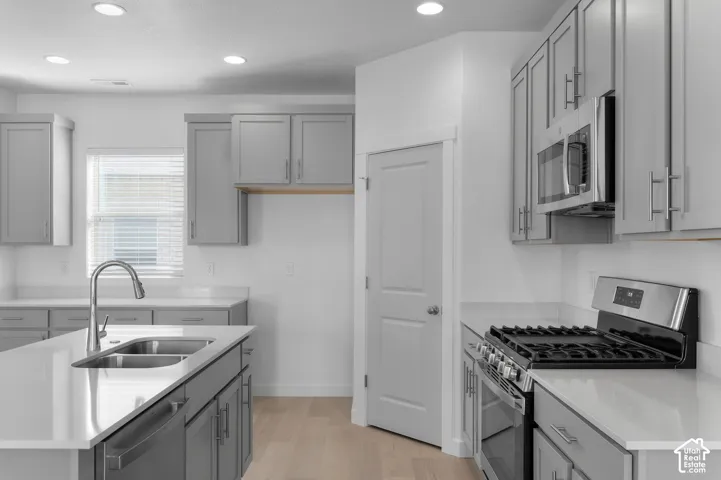 Kitchen featuring grey cabinetry, quartz countertops, a central island with an undermount dual-basin sink, stainless steel gas range, and recessed lighting